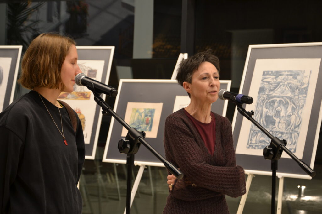 Dyrektor MBP i autorka wystawy przy mikrofonach. W tle sztalugi z grafikami.