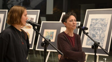 Dyrektor MBP i autorka wystawy przy mikrofonach. W tle sztalugi z grafikami.