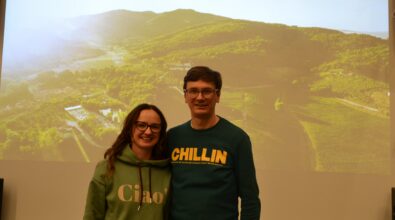 Karolina Iskierka i Paweł Sierszeń stoją przed dużym ekranem projekcyjnym z wyświetlonym slajdem przedstawiającym krajobraz z winnicą. Oboje uśmiechają się do aparatu. Za nimi widoczny jest tytuł prezentacji „Jak adoptowaliśmy kawałek winnicy? – Palagina”. Prelegenci pozują do zdjęcia na scenie w