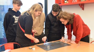 Na zdjęciu widać grupę nastolatków. Jeden z nich, mający czarną bluzę, trzyma w dłoni pipetę. Nalew wodę na ziemię położoną na szkiełku mikroskopowym, tworząc próbkę do badań. Reszta nastolatków uważnie się przygląda. Na ścianie po prawej stronie wisi czerwona półka. Zdjęcie własnością MBP Piotrków.