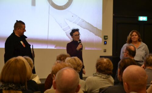 Na zdjęciu widoczna jest pani dyrektor Mediateki 800-lecia przemawiająca do zgromadzonej publiczności. Stoi przed ekranem projekcyjnym, trzyma mikrofon i zwraca się do uczestników wydarzenia siedzących na sali.