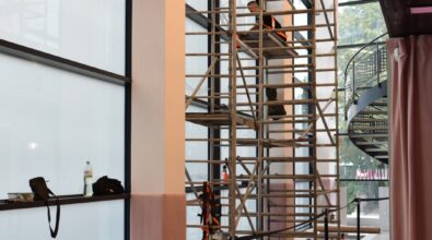 Widok wnętrza nowoczesnego budynku z rusztowaniem i sprzętem – prace techniczne realizowane w ramach projektu wspieranego przez fundusze europejskie. Na dole zdjęcia widoczne są logotypy instytucji wspierających projekt.