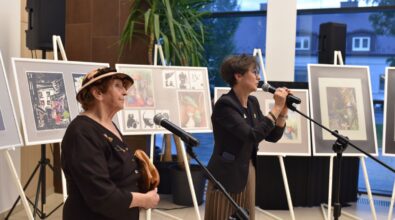 Dyrektor MBP i autorka wystawy stoją przy mikrofonach. W tle widać prace na sztalugach.