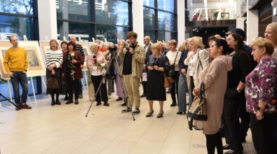 Na zdjęciu widoczna są uczestnicy zgromadzeni w przestrzeni wystawowej podczas otwarcia wystawy, stojący i słuchający wystąpienia. W tle widoczne są plansze z prezentowanymi pracami, a kadr oddaje uroczysty i integrujący charakter wydarzenia kulturalnego.