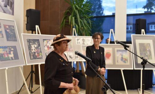 Dyrektor MBP i autorka wystawy stoją przy mikrofonach. W tle widać prace na sztalugach.