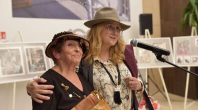 Na zdjęciu widoczne są dwie kobiety stojące przy mikrofonie podczas otwarcia wystawy, obejmujące się i uśmiechające do zgromadzonych gości. Scena dokumentuje symboliczny moment podsumowania wydarzenia i podkreśla serdeczną, wspólnotową atmosferę spotkania.