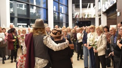 Artystka pozuje z uczestniczką wydarzenia, stoją blisko siebie, obejmując się ramieniem. W tle widoczni są inni uczestnicy wernisażu.