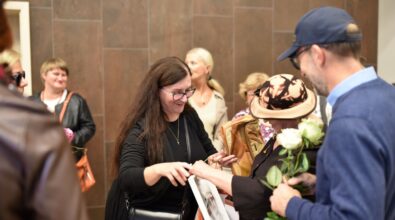 Na zdjęciu widoczny jest moment wręczania kwiatów i upominku artystce po otwarciu wystawy. W tle znajdują się uczestnicy wydarzenia, a cała scena oddaje serdeczną i uroczystą atmosferę spotkania kulturalnego.