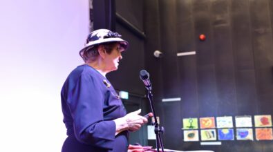 Na zdjęciu widoczna jest artystka stojąca przy mikrofonie i czytająca tekst podczas spotkania autorskiego. Ujęcie z boku podkreśla skupienie prowadzącej oraz oficjalny, literacki charakter wydarzenia kulturalnego.