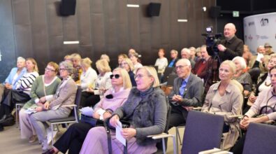 Na zdjęciu widoczna jest publiczność zgromadzona na sali podczas spotkania autorskiego, siedząca na krzesłach i uważnie słuchająca wystąpienia. Uczestnicy trzymają programy lub książki, a kadr oddaje spokojną i skupioną atmosferę wydarzenia kulturalnego.