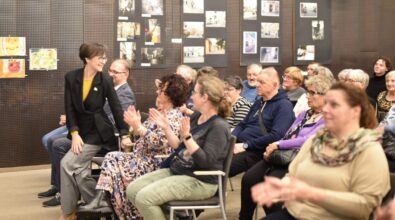 Na zdjęciu widoczna jest publiczność zgromadzona na sali podczas wydarzenia kulturalnego, siedząca na krzesłach i nagradzająca uczestników brawami. W tle znajdują się plansze z fotografiami prezentowanymi na wystawie, a atmosfera spotkania ma charakter uroczysty i integrujący lokalną społeczność.