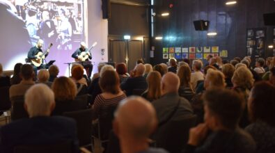 Na zdjęciu widać liczną publiczność siedzącą na krzesłach w sali bibliotecznej, skierowaną w stronę ekranu projekcyjnego oraz prowadzącego wydarzenie. Uczestnicy uważnie oglądają prezentację, a całość przedstawia wykład lub spotkanie kulturalne odbywające się w przestrzeni Mediateki.