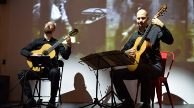 Na zdjęciu widoczni są dwaj gitarzyści siedzący na scenie podczas koncertu muzyki filmowej, grający na gitarach klasycznych. Przed nimi ustawione są pulpity z nutami, a w tle wyświetlana jest projekcja filmowa, która podkreśla artystyczny i audiowizualny charakter wydarzenia.