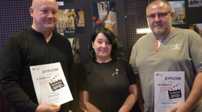 Zdjęcie laureatów z dyplomami na tle wystawy ze zdjęć.