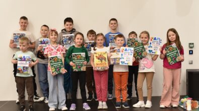 Grupa dzieci stoi na scenie w Mediatece 800-lecia, prezentując otrzymane nagrody i dyplomy. Uczestnicy trzymają w dłoniach książki popularnonaukowe, m.in. encyklopedie dla dzieci, oraz pamiątkowe dyplomy potwierdzające udział w zajęciach. Dzieci z dumą pozują do wspólnego zdjęcia, podsumowując tydzień pełen aktywności, nauki i kreatywnej zabawy podczas ferii w Mediatece.