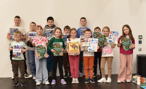 Grupa dzieci stoi na scenie w Mediatece 800-lecia, prezentując otrzymane nagrody i dyplomy. Uczestnicy trzymają w dłoniach książki popularnonaukowe, m.in. encyklopedie dla dzieci, oraz pamiątkowe dyplomy potwierdzające udział w zajęciach. Dzieci z dumą pozują do wspólnego zdjęcia, podsumowując tydzień pełen aktywności, nauki i kreatywnej zabawy podczas ferii w Mediatece.