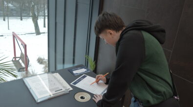 Chłopiec wypełniająca kartę pracy przy stanowisku edukacyjnym. Obok znajdują się materiały informacyjne oraz elementy instalacji służącej do wykonywania zadania. Uczestnik zapisuje odpowiedzi, analizując wcześniej wykonane doświadczenie lub obserwację.