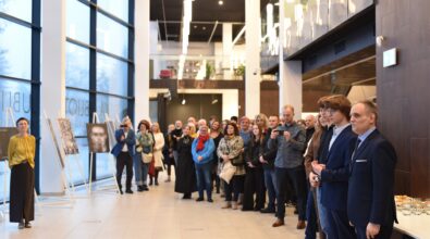 W przestronnym holu Mediateki 800-lecia zgromadzili się uczestnicy otwarcia wystawy fotografii uczniów i absolwentów Zespołu Szkół Ponadpodstawowych nr 5 w Piotrkowie Trybunalskim „Fototechnika”. Po prawej stronie stoją zaproszeni goście w eleganckich strojach, a za nimi liczna publiczność uważnie słucha przemówienia. Po lewej stronie widoczne są fotografie prezentowane na sztalugach, ustawione wzdłuż przeszklonej ściany budynku. W tle widać nowoczesne, jasne wnętrze Mediateki z wysokimi oknami i antresolą.