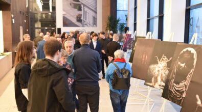 Uczestnicy otwarcia wystawy fotografii „Fototechnika” w Mediatece 800-lecia oglądają prace uczniów i absolwentów Zespołu Szkół Ponadpodstawowych nr 5 w Piotrkowie Trybunalskim. Wzdłuż przeszklonej ściany ustawione są na sztalugach wielkoformatowe fotografie, w tym portrety oraz dynamiczne ujęcia postaci w ruchu. Goście spacerują między ekspozycjami, zatrzymują się przy wybranych pracach i prowadzą rozmowy. Jasne, nowoczesne wnętrze Mediateki z wysokimi oknami i antresolą stanowi tło wydarzenia.