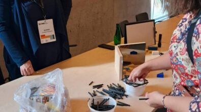 dwie kobiety stojące przy stoliku. Jedna z nich dotyka rzeczy znajdujących się na stole, które służą do przeprowadzania eksperymentów.