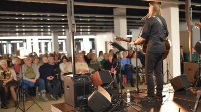 Widok na muzyków oraz publiczność. Dwóch gitarzystów widocznych od tyłu wykonuje utwór na scenie. Przed nimi stoją mikrofony, monitory odsłuchowe oraz pedały efektów. W tle widać siedzącą publiczność.