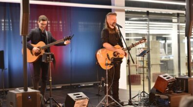 Dwóch muzyków gra na scenie na gitarach. Przed nimi stoją mikrofony, monitory odsłuchowe oraz pedały efektów.