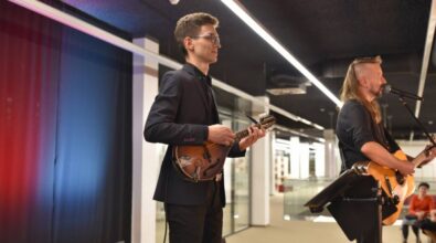 Zbliżenie na muzyków. Mężczyzna w długich włosach gra na gitarze i śpiewa, drugi mężczyzna gra na mandolinie.