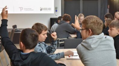 Uczestnicy siedzią przy stolikach, niektórzy zgłaszają się do odpowiedzi. Na ekranie w tle widoczne są logotypy organizatorów: Piotrkowa Trybunalskiego i Biblioteki.