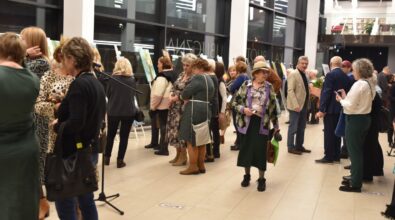 wernisaż wystawy malarskiej, odbywający się w eleganckim, przestronnym wnętrzu z dużymi oknami. Na ścianach i sztalugach rozmieszczone są różnorodne obrazy, które przyciągają uwagę zgromadzonych gości. Widzowie, w różnym wieku, przyglądają się eksponatom, niektórzy w skupieniu analizują detale dzieł sztuki. W tle widać żywą atmosferę, a światło oświetla zarówno prace, jak i osoby uczestniczące w wydarzeniu.