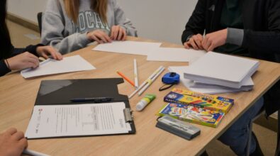 Uczestnicy konkursu „GEOinżynieria” siedzą przy stole, na którym znajdują się materiały biurowe i plastyczne. Na blacie widoczne są kartki papieru, kolorowa plastelina, mazaki, długopisy, linijki oraz folder z wydrukowanymi dokumentami. Uczestnicy składają kartki papieru, pracując w zespołach. Atmosfera skupienia sugeruje intensywną pracę nad zadaniami matematycznymi.