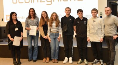 Grupa osób pozuje do zdjęcia na tle ekranu z napisem 