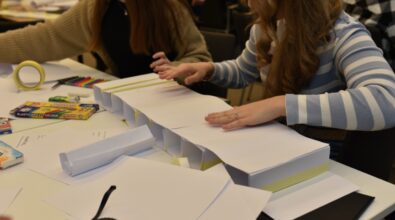 Dwie uczennice pracują nad modelem konstrukcji mostu z papieru w ramach konkursu „GEOinżynieria”. Na stole leżą materiały plastyczne, taśma klejąca, kolorowe mazaki, plastelina i linijka. Widoczny jest częściowo złożony most wykonany z kartki papieru, wzmocniony taśmą. Dziewczyny skupione są na dokładnym składaniu i dopasowywaniu elementów.