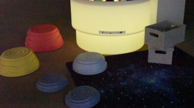 Na zdjęciu widoczny jest kącik sensoryczny utworzony w Mediatece 800-lecia w ramach działań Inkluzoteki. W jego centrum znajduje się podświetlany stół sensoryczny z zestawem różnorodnych pomocy stymulujących zmysły. Obok ustawiono elementy mobilnej ścieżki sensorycznej oraz dywan sensoryczny o świetlnej, gwiezdnej strukturze.