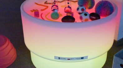 Na zdjęciu widoczny jest podświetlany stół sensoryczny stanowiący element kącika sensorycznego utworzonego w Mediatece 800-lecia w ramach działań Inkluzoteki. Na jego powierzchni znajdują się różnorodne pomoce sensoryczne o zróżnicowanych kształtach, i kolorach.