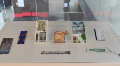 Na zdjęciu znajduje się wystawa prezentowana w gablocie. W jej wnętrzu znajduje się zbiór różnorodnych zakładek do książek, które wykonane są z różnych materiałów i przedstawiają różnorodne wzory. Niektóre zakładki mają motywy architektoniczne, inne zawierają ilustracje, a jeszcze inne ukazują motywy literackie. Zakładki są starannie ułożone, a centralny element to trzy zakładki umieszczone w przezroczystej pionowej ramce. Całość jest umieszczona w szklanej gablocie, co nadaje eksponatom charakteru wystawowego.