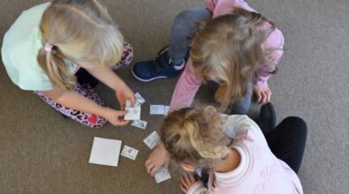 Dzieci siedzące na podłodze skupiają się na układaniu małych karteczek. Są w swobodnych ubraniach, pokazując pracę zespołową, gdy wspólnie rozwiązują zadanie. Scena przekazuje poczucie skupienia i zabawy.