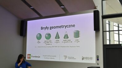 Prezentacja na temat brył geometrycznych wyświetlana na dużym ekranie. Zawiera ilustracje i wzory dotyczące kuli, odcinka kulistego, stożka, stożka ściętego oraz walca. Na dole ekranu logotypy organizatorów i sponsorów: Fundacja mBanku, Piotrków Trybunalski oraz Biblioteka w Piotrkowie Trybunalskim. Po lewej stronie kobieta w niebieskiej bluzce trzyma mikrofon, stojąc obok ekranu w nowoczesnym wnętrzu z przeszklonymi ścianami