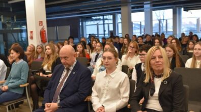 Publiczność siedząca w jasnej sali konferencyjnej. W pierwszych rzędach widoczni są młodzi ludzie oraz osoby dorosłe, w tle zaś widać okna z widokiem na budynki miasta. W sali znajdują się białe filary i ciemny sufit z elementami technicznymi.