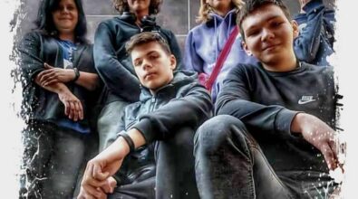 Na zdjęciu widoczna jest grupa sześciu osób pozujących przed szarym, gładkim tłem. Osoby stoją w różnych pozach, na przodzie dwóch młodych mężczyzn siedzi na ugiętych nogach, podczas gdy pozostali stoją za nimi. Zdjęcie ma artystyczną ramkę w stylu rozpryskującej się farby, która dodaje dynamicznego efektu. Grupa wygląda na zgraną, a ich różnorodne wyrazy twarzy wskazują na przyjazną atmosferę. Ubrania osób mają głównie ciemne kolory, co kontrastuje z jasną ramką zdjęcia.