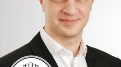 Portret mężczyzny w ciemnej marynarce na białym tle. W lewym dolnym rogu zdjęcia znajduje się logo z napisem „Krukowski Day” oraz stylizowanym motywem piszczałek organowych.