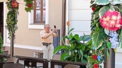 Na pierwszy planie ogródek letni przy restauracji lub pubie. Widać stoliki i krzesełka oraz kwiaty przywiązane do konstrukcji. W tle na chodniku stoi mężczyzna i robi zdjęcia telefonem.