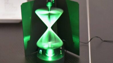 świecąca na zielono instalacja przypominająca klepsydrę. Składa się z wirujących elementów, które tworzą efekt świetlny w kształcie dwóch połączonych stożków. Całość jest umieszczona w ciemnej obudowie z zielonymi ściankami, a urządzenie stoi na stole.