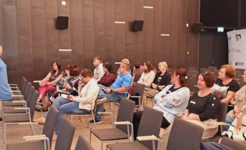 W sali widać siedzących uczestników szkolenia przed którymi stoi osoba prowadząca.