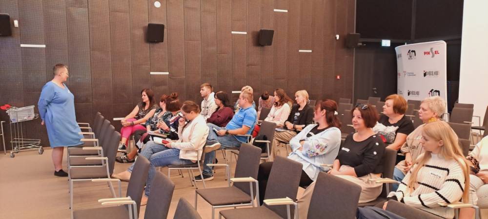 W sali widać siedzących uczestników szkolenia przed którymi stoi osoba prowadząca.