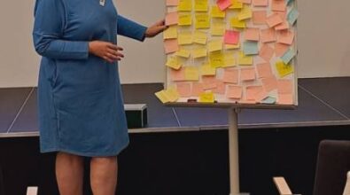 Osoba prowadząca stoi przy tablicy flipchart, na której znajduje się dużo zapisanych karteczek samoprzylepnych.