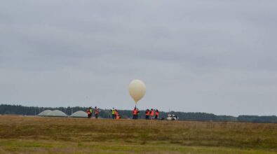 Zdjęcie przedstawia grupę osób w kamizelkach odblaskowych na otwartym terenie, przygotowujących się do wypuszczenia dużego balonu meteorologicznego.