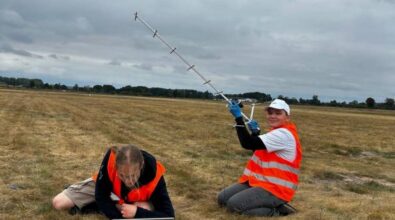 Na zdjęciu widoczne są dwie osoby w pomarańczowych kamizelkach odblaskowych, które znajdują się na otwartym terenie. Jedna osoba obsługuje laptopa, a druga trzyma antenę kierunkową, prawdopodobnie do odbioru sygnału radiowego z balonu meteorologicznego.