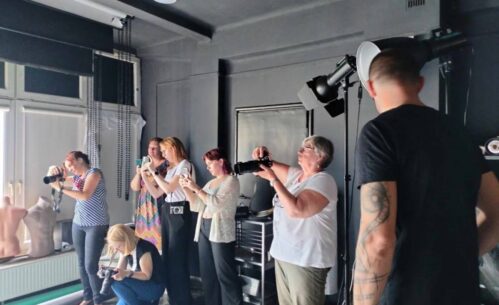 Zdjęcie przedstawia grupę ludzi w studio fotograficznym, skoncentrowanych na robieniu zdjęć.