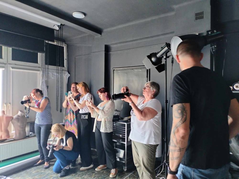 Zdjęcie przedstawia grupę ludzi w studio fotograficznym, skoncentrowanych na robieniu zdjęć.