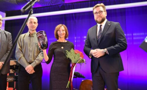 Laureatka konkursu stoi na scenie z prezydentem Piotrkowa Tryb. oraz osobami z jury. Wszyscy pozują do zdjęcia. Główna zwyciężczyni trzyma w rekach bukiet oraz rubinowy wazon.